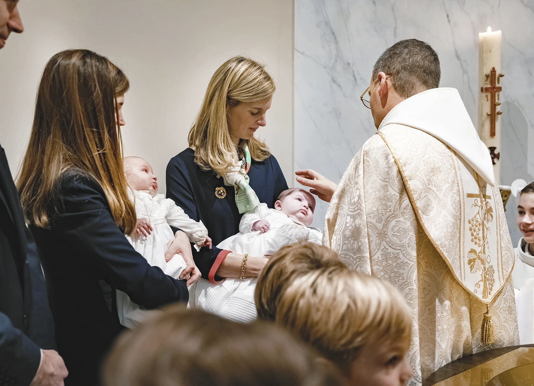 Le prêtre bénit le deuxième bébé avec une expression douce et solennelle.