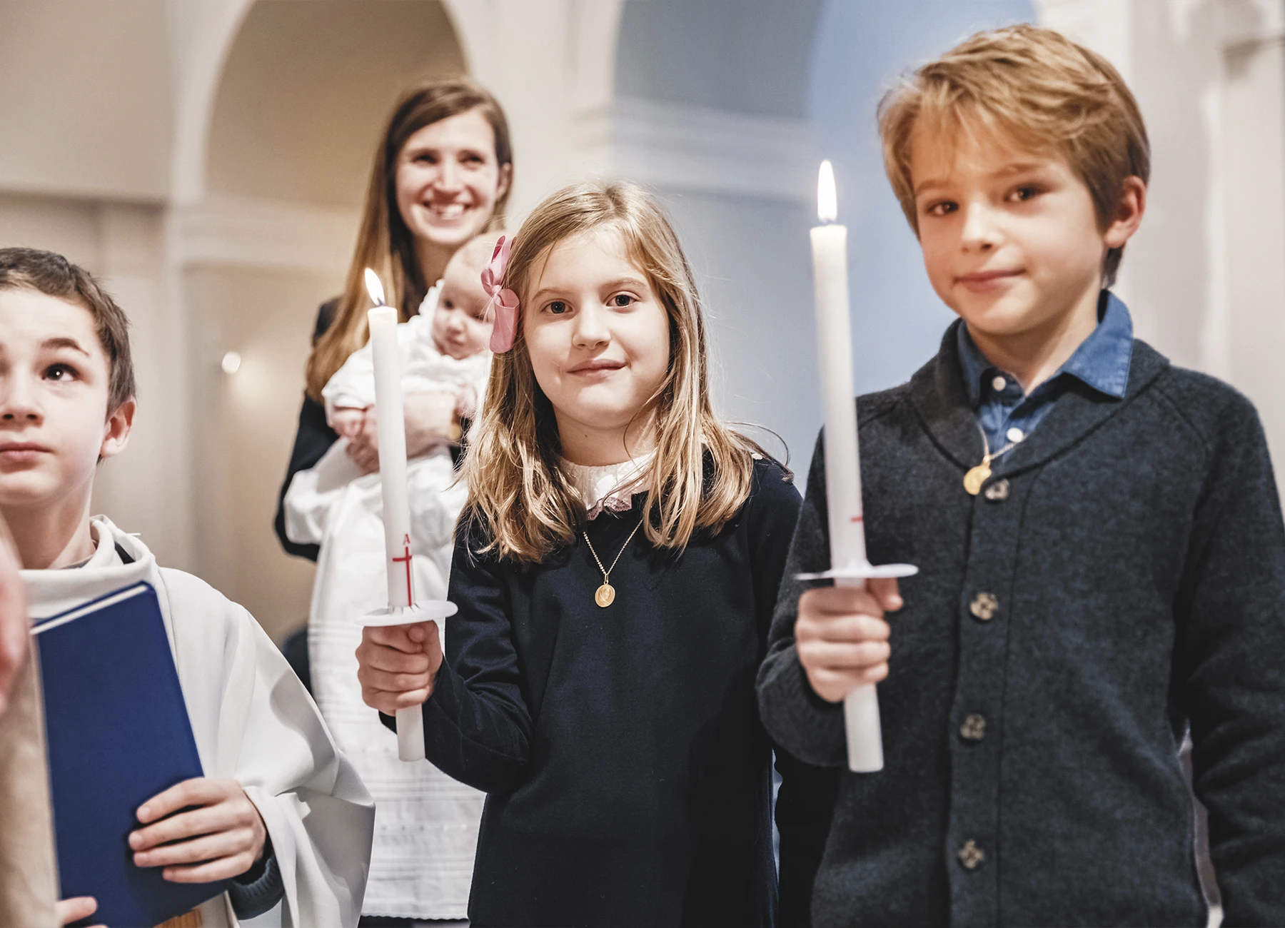 Deux enfants, un garçon et une fille, tenant des cierges lors du baptême à la Paroisse Notre-Dame de l’Assomption de Passy.