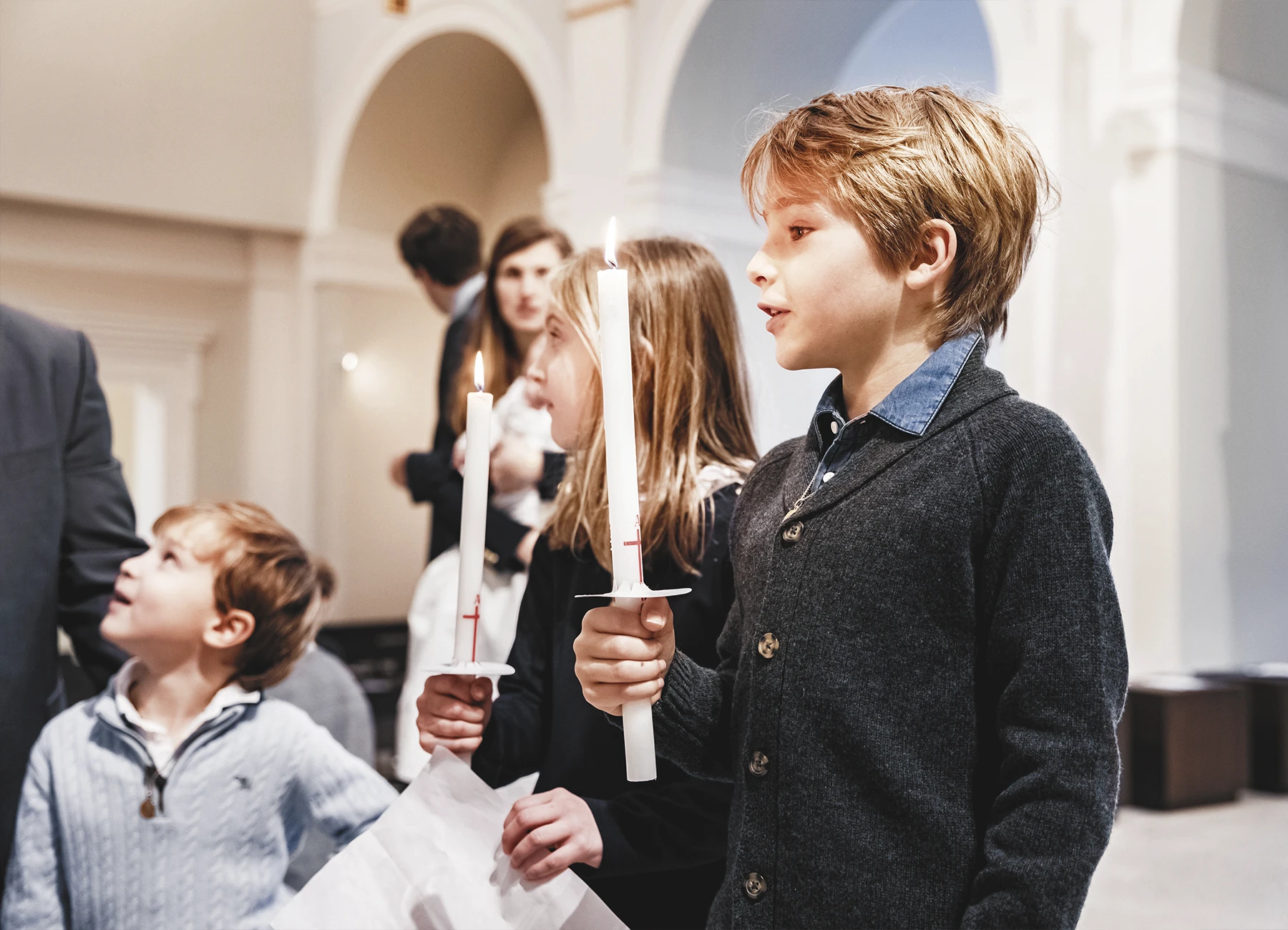 Deux enfants, un garçon et une fille, tenant des cierges lors du baptême à la Paroisse Notre-Dame de l’Assomption de Passy.