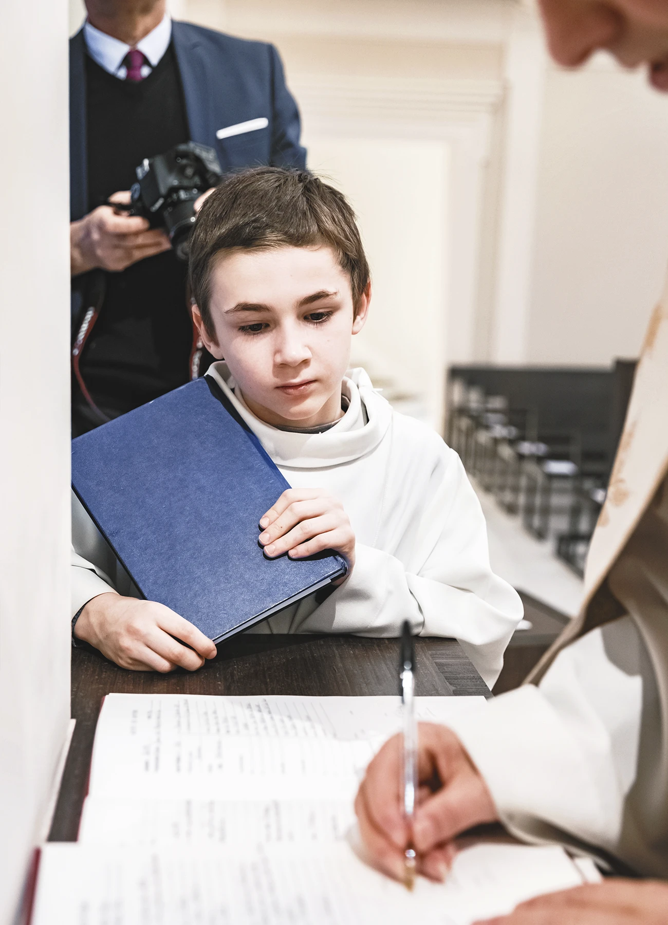 Un enfant de chœur observe attentivement le prêtre signant le registre.