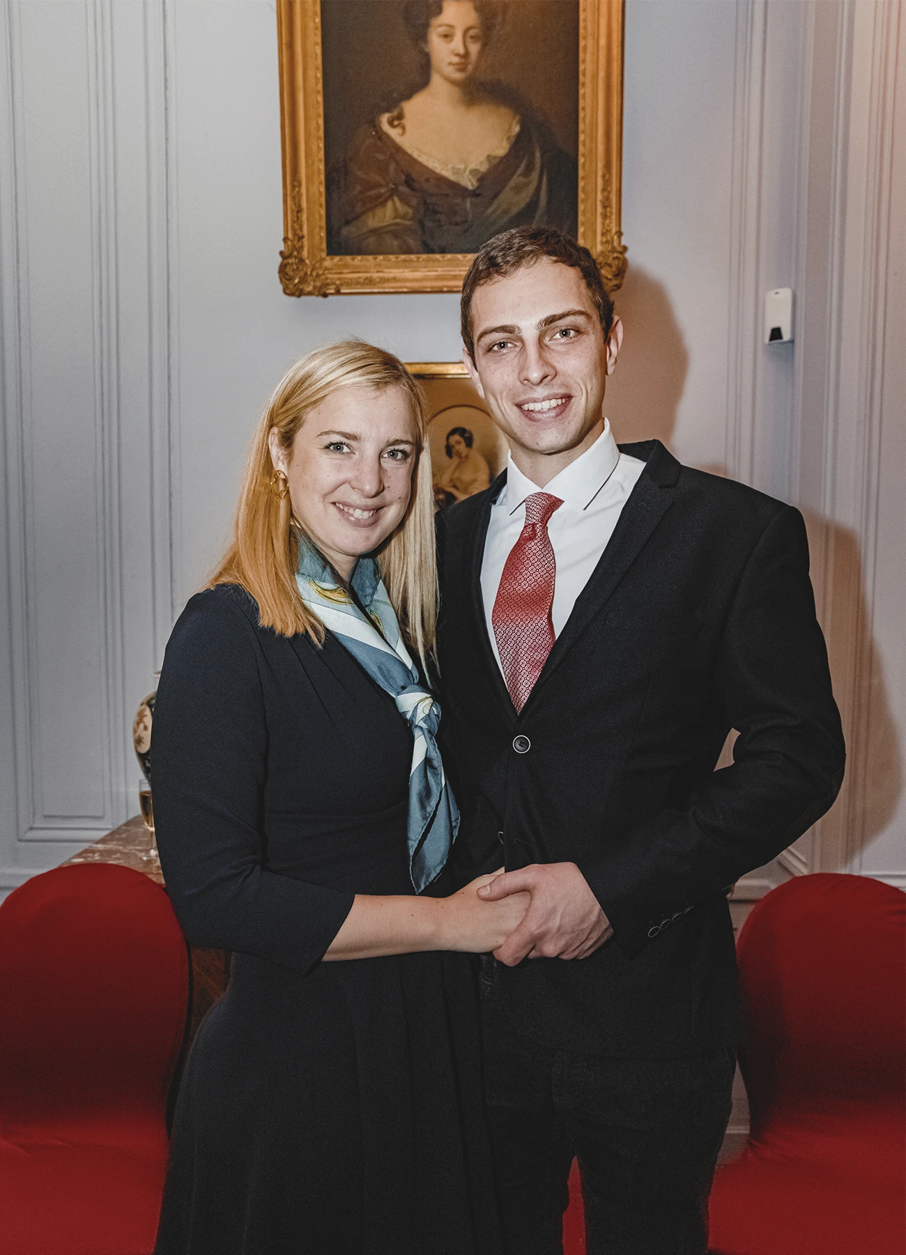 Couple élégant lors de la soirée d’anniversaire, l’homme en costume avec une cravate rouge et la femme en tenue noire avec un foulard bleu.