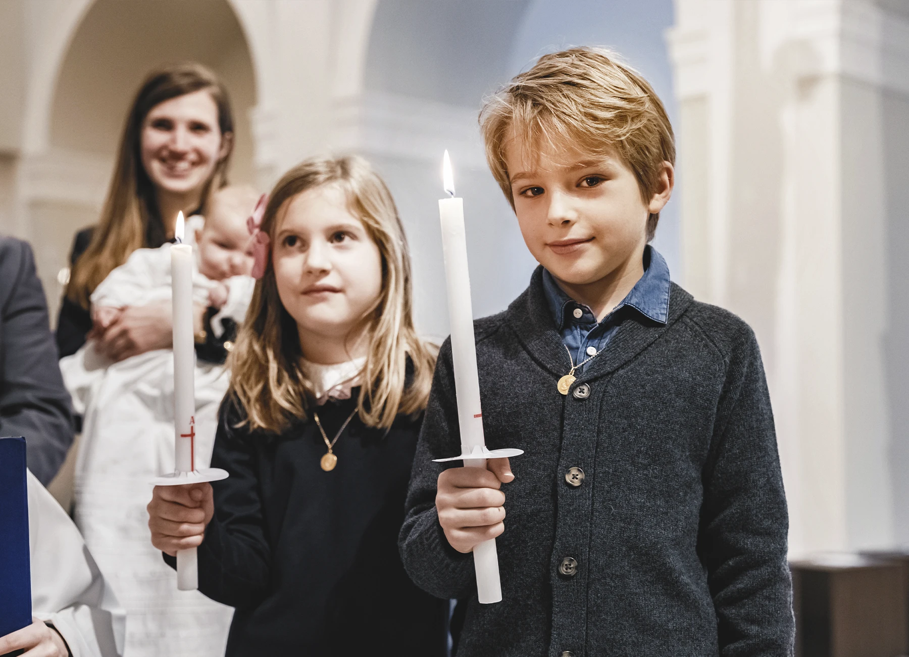 Deux enfants, un garçon et une fille, tenant des cierges lors du baptême à la Paroisse Notre-Dame de l’Assomption de Passy.