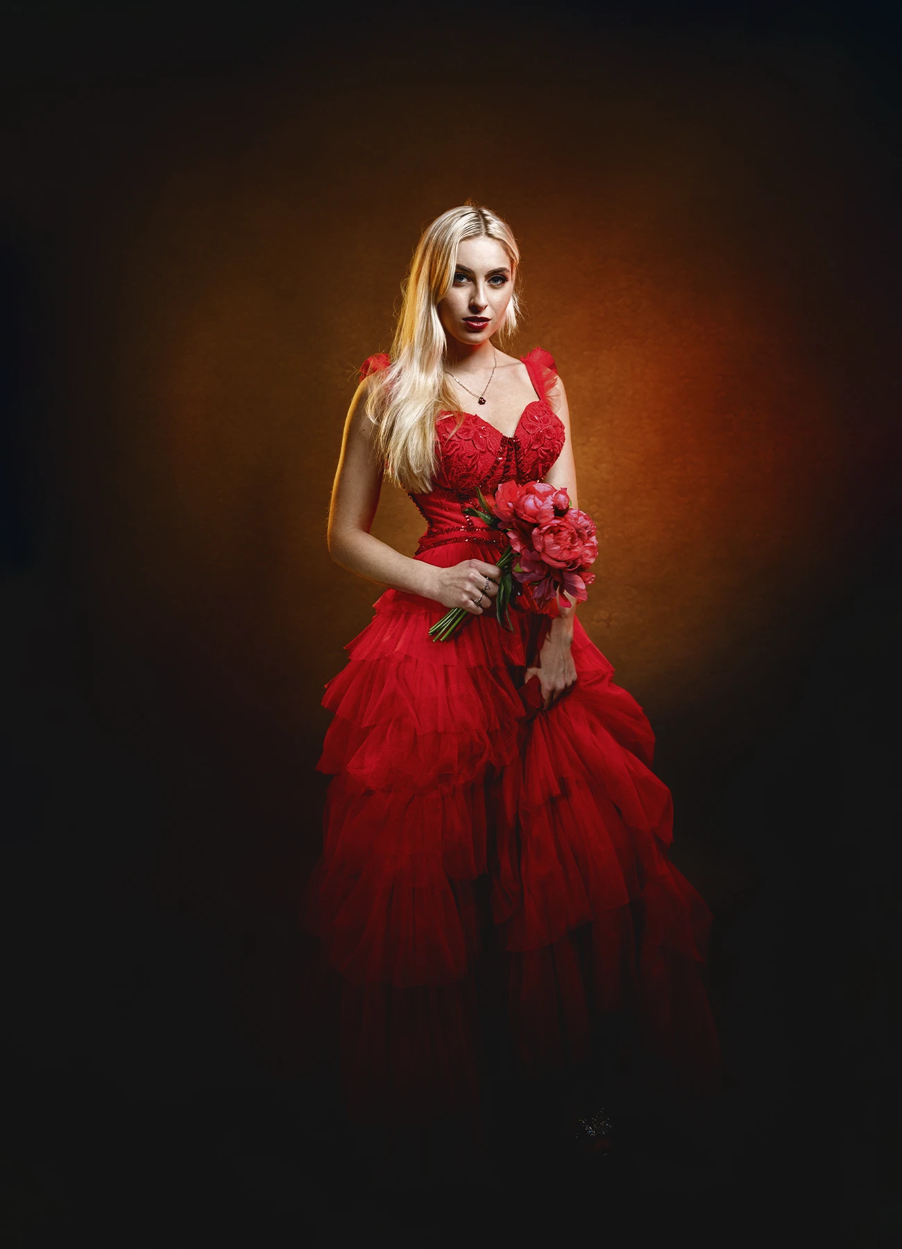 Candice en robe de tulle rouge, debout, tenant un bouquet de fleurs.