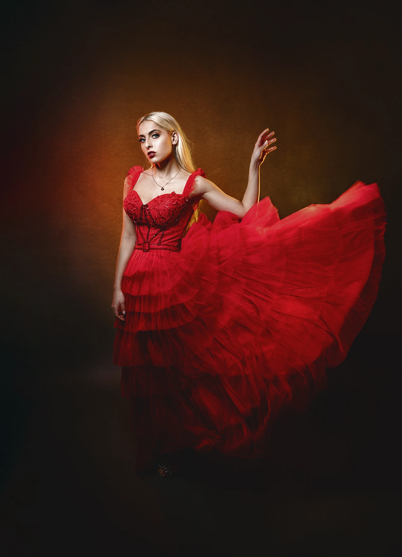 Candice en robe de soirée rouge, face à la caméra, jouant avec les volants de sa robe.