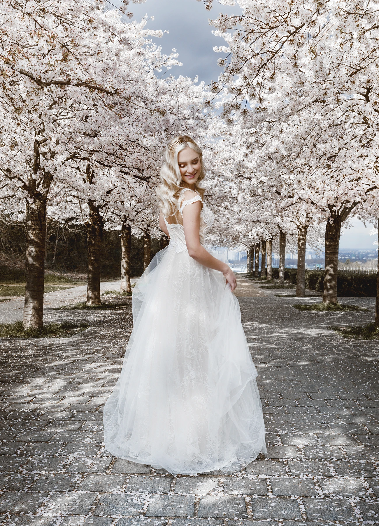 Eva Mikulski en robe de mariée blanche, jouant avec les volants sous les cerisiers en fleurs