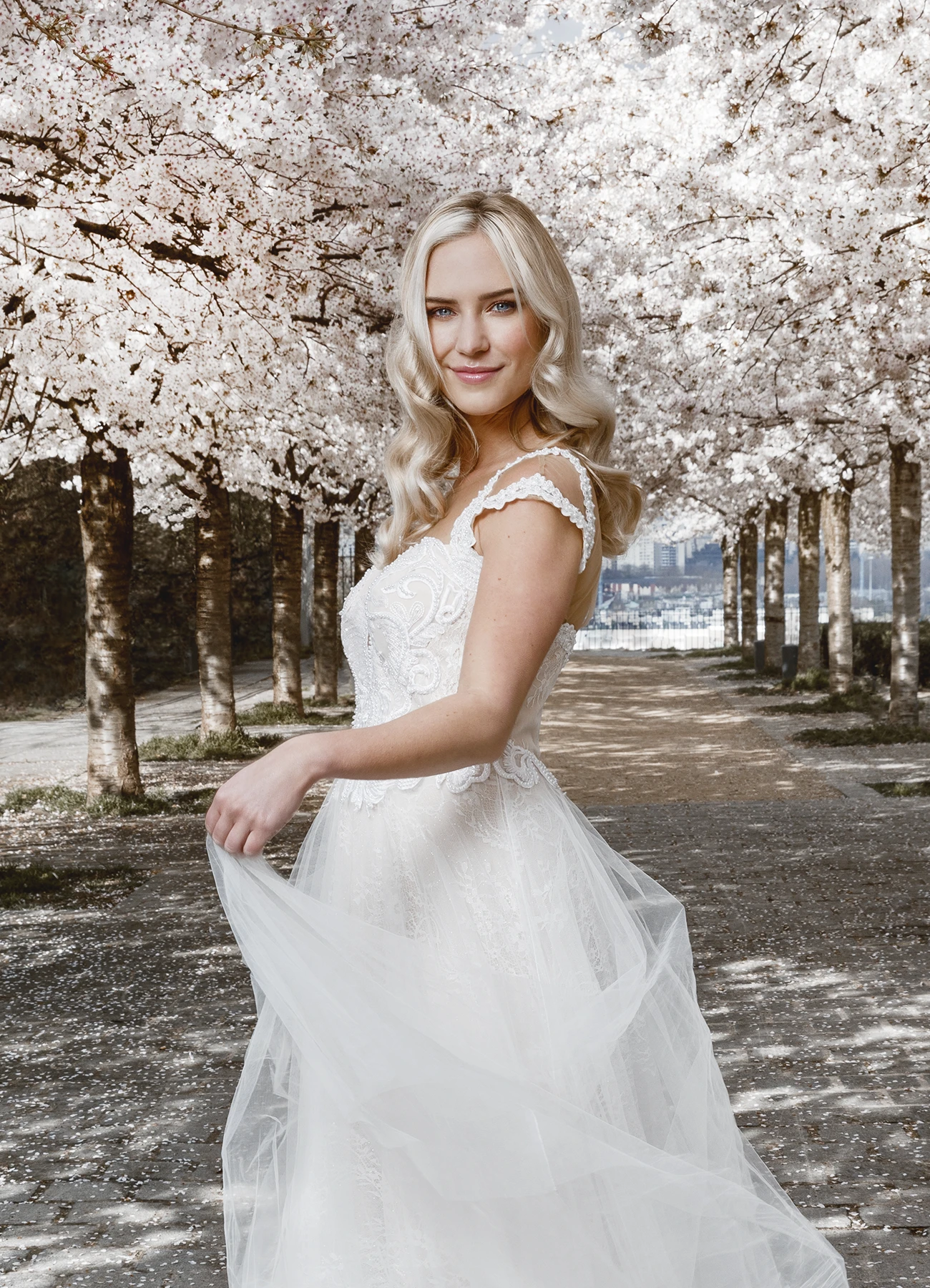 Eva Mikulski, en robe blanche Elyssa Couture Paris, entourée de cerisiers en fleurs