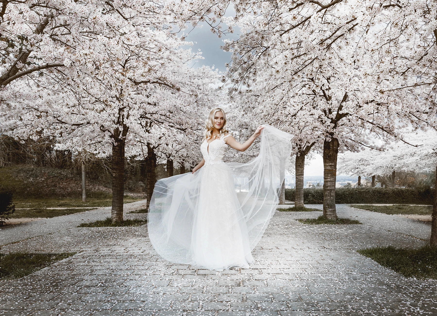 Eva Mikulski en robe de mariée blanche jouant avec sa robe sous les cerisiers en fleurs