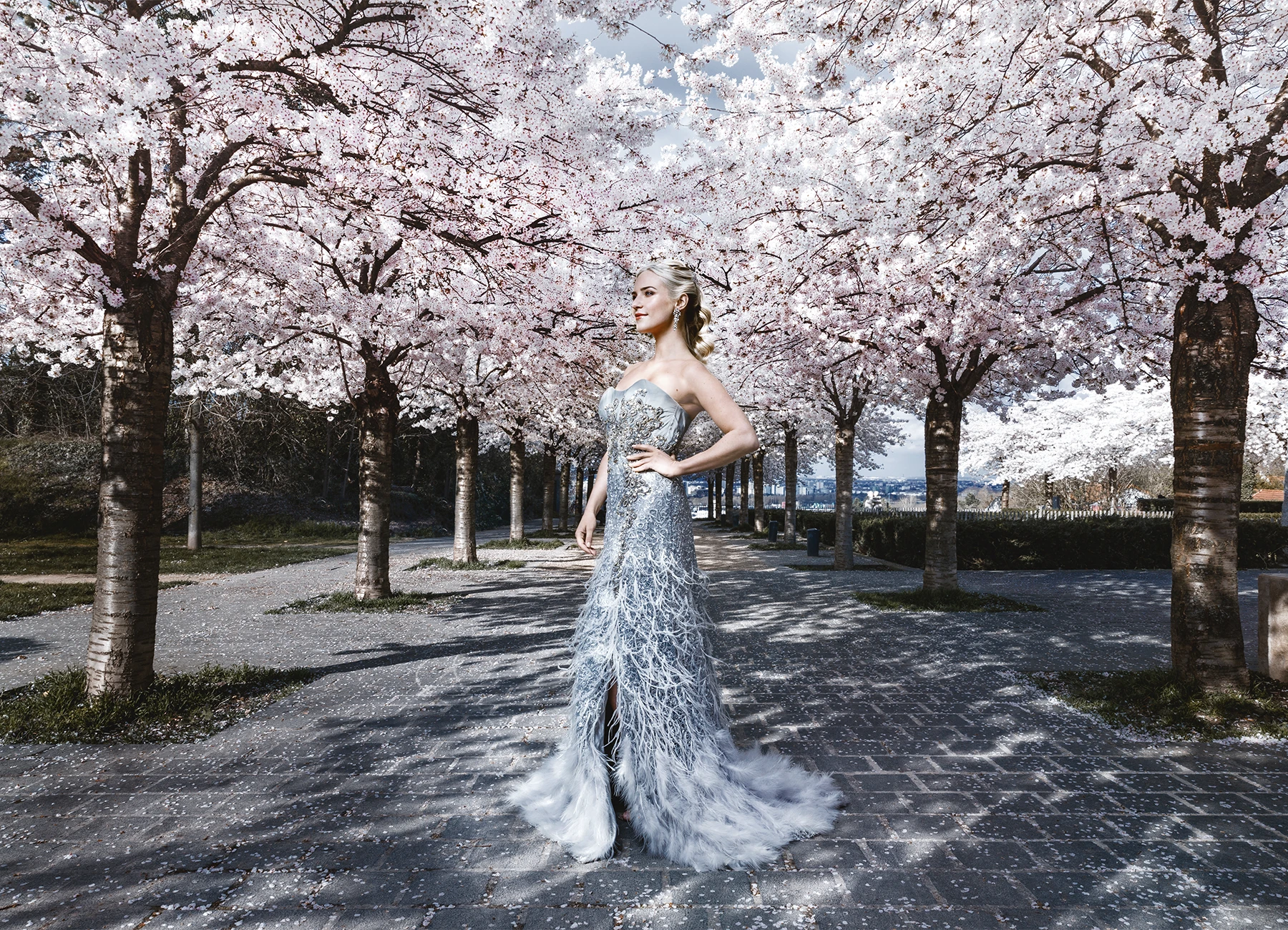 Eva Mikulski en robe de soirée grise Elyssa Couture, souriant de profil sous les cerisiers en fleurs