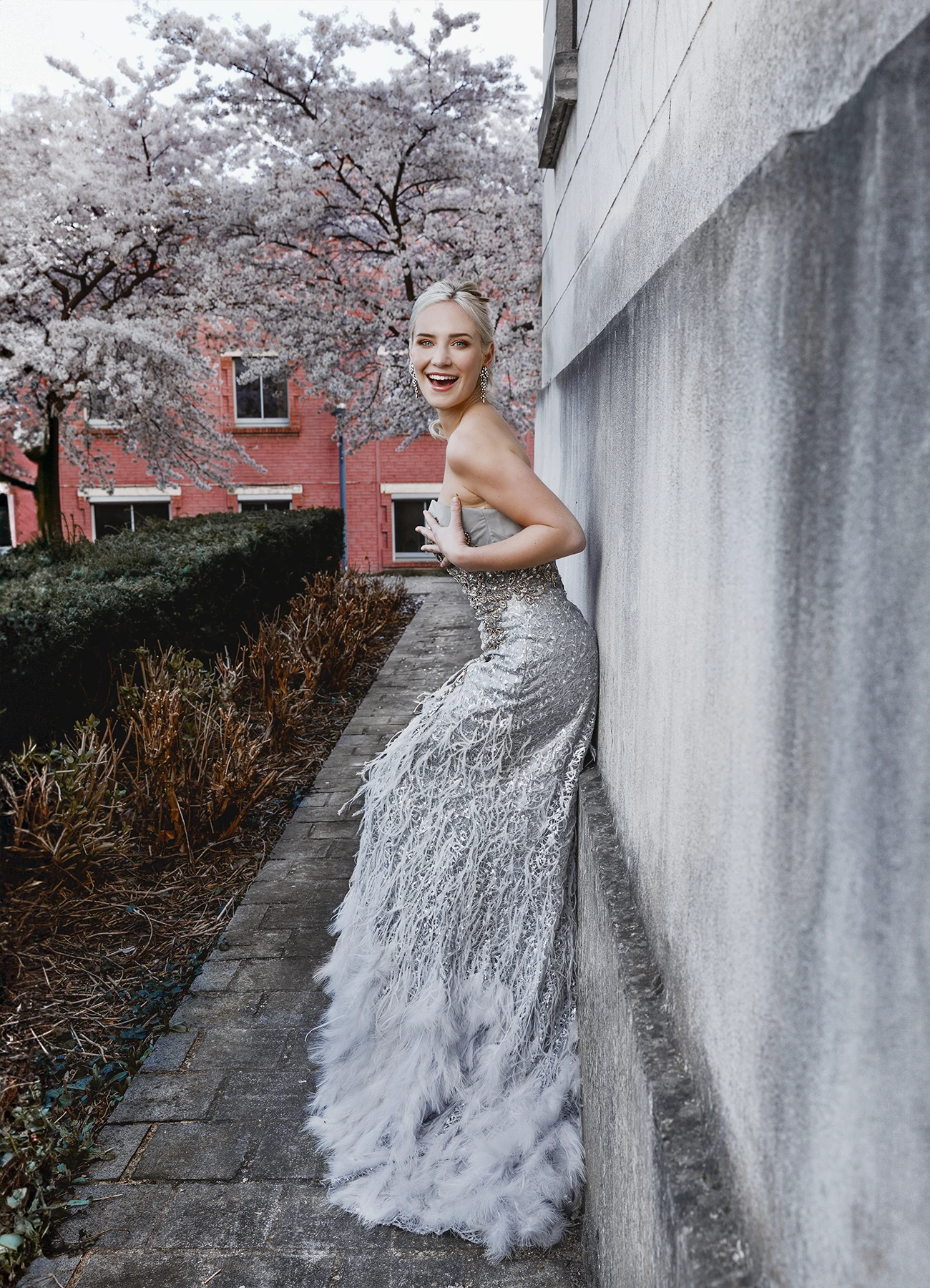 Portrait d'Eva Mikulski en robe de soirée grise, riant devant l'objectif dans une allée