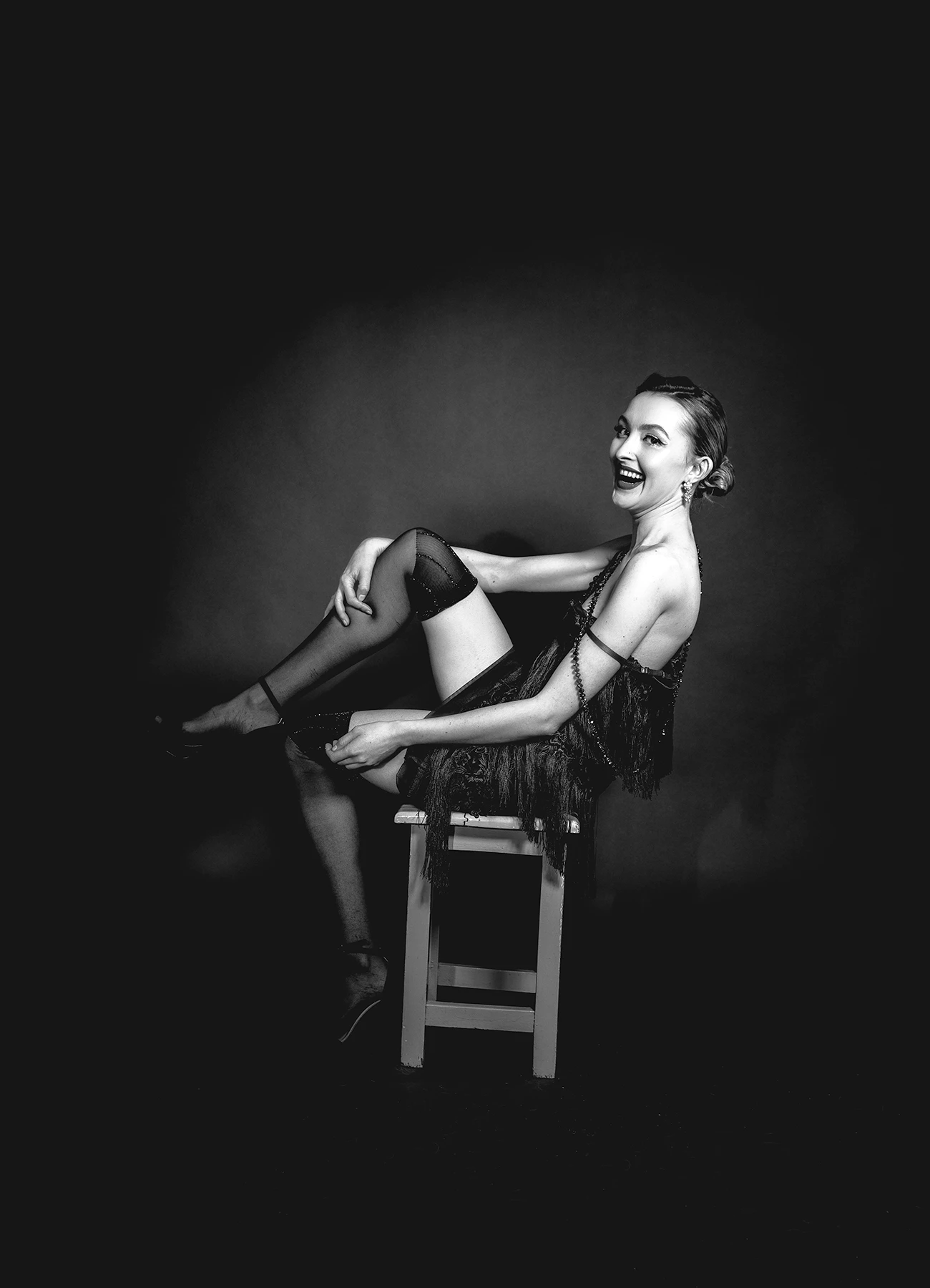 Kalysta en bas et robe style années 20, assise sur un tabouret dans un studio riant lors d'un hommage à Marlene Dietrich, photographie réalisée par Laurène Zabary.