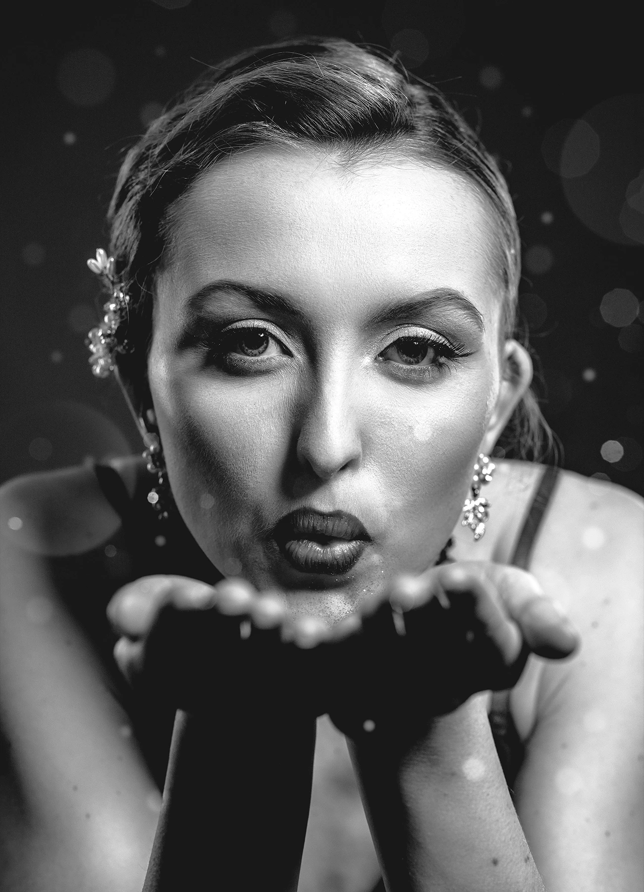 Portrait serré de Kalysta soufflant des paillettes vers l’objectif, photo en noir et blanc réalisée en studio par Laurène Zabary.