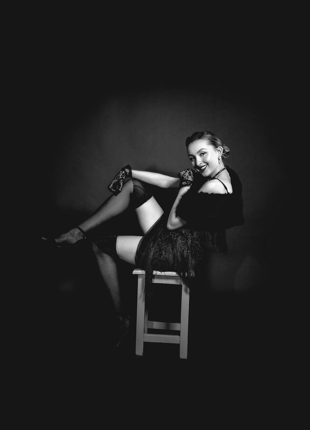 Kalysta en bas et robe style années 20, posant de manière espiègle sur un tabouret, inspirée de Marlène Dietrich, photographie réalisée par Laurène Zabary en studio.