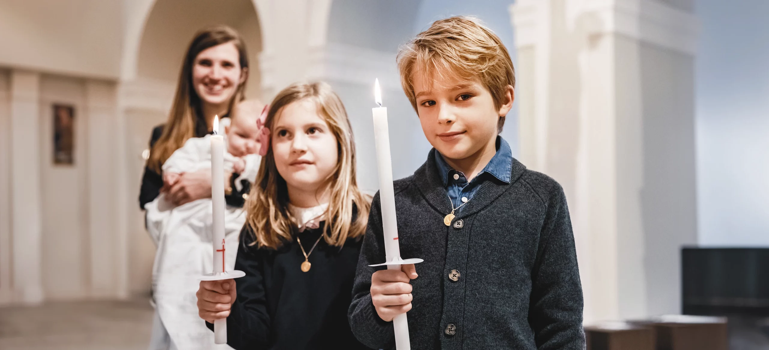 Deux enfants, un garçon et une fille, tenant des cierges lors du baptême à la Paroisse Notre-Dame de l’Assomption de Passy.