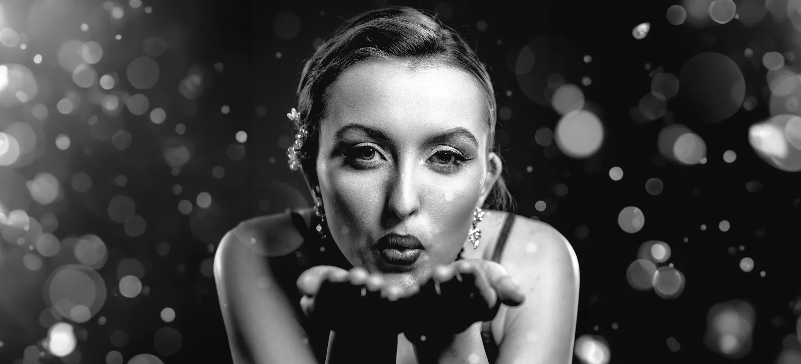 Portrait serré de Kalysta soufflant des paillettes vers l’objectif, photo en noir et blanc réalisée en studio par Laurène Zabary.