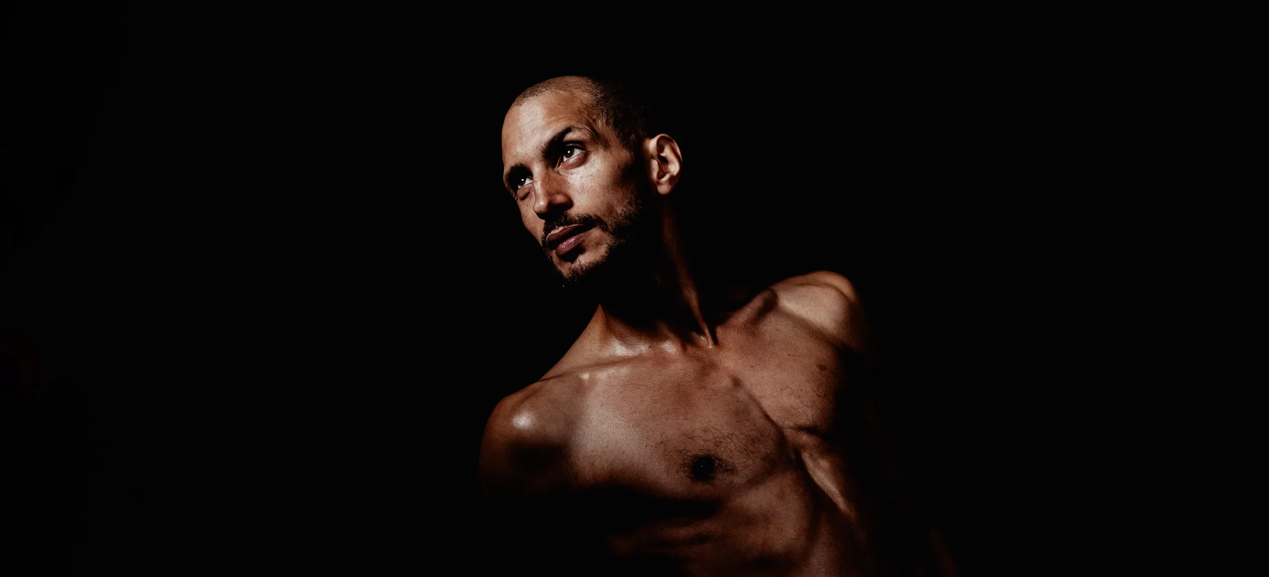 Portrait contrasté d’un comédien sur fond noir, regardant au loin avec intensité.