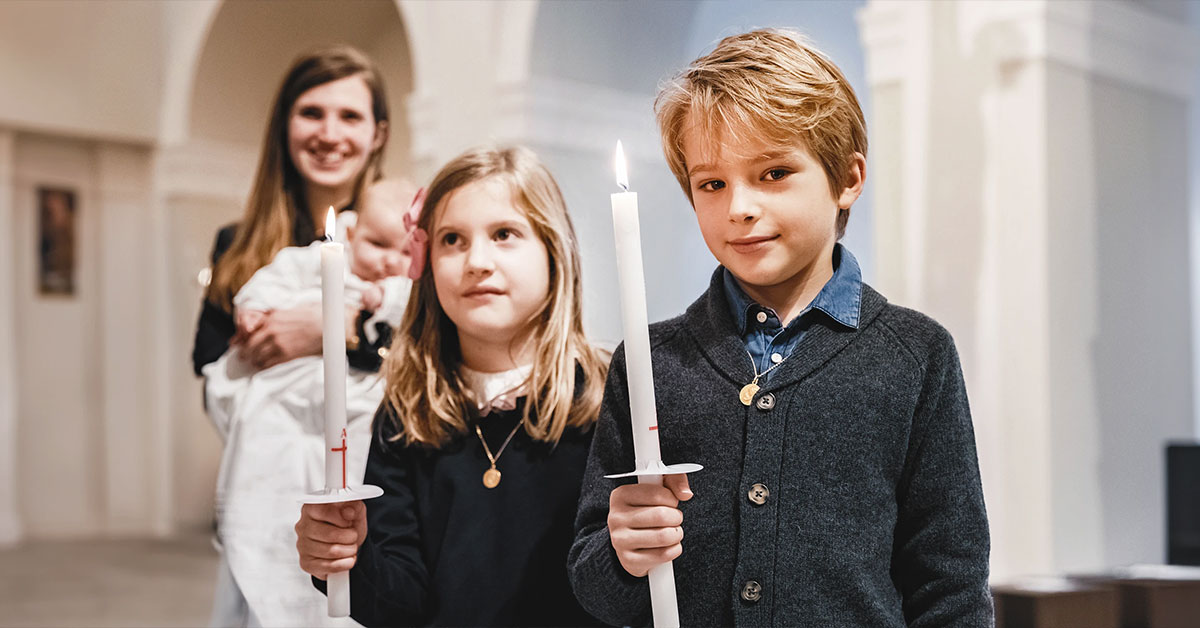 Deux enfants, un garçon et une fille, tenant des cierges lors du baptême à la Paroisse Notre-Dame de l’Assomption de Passy.