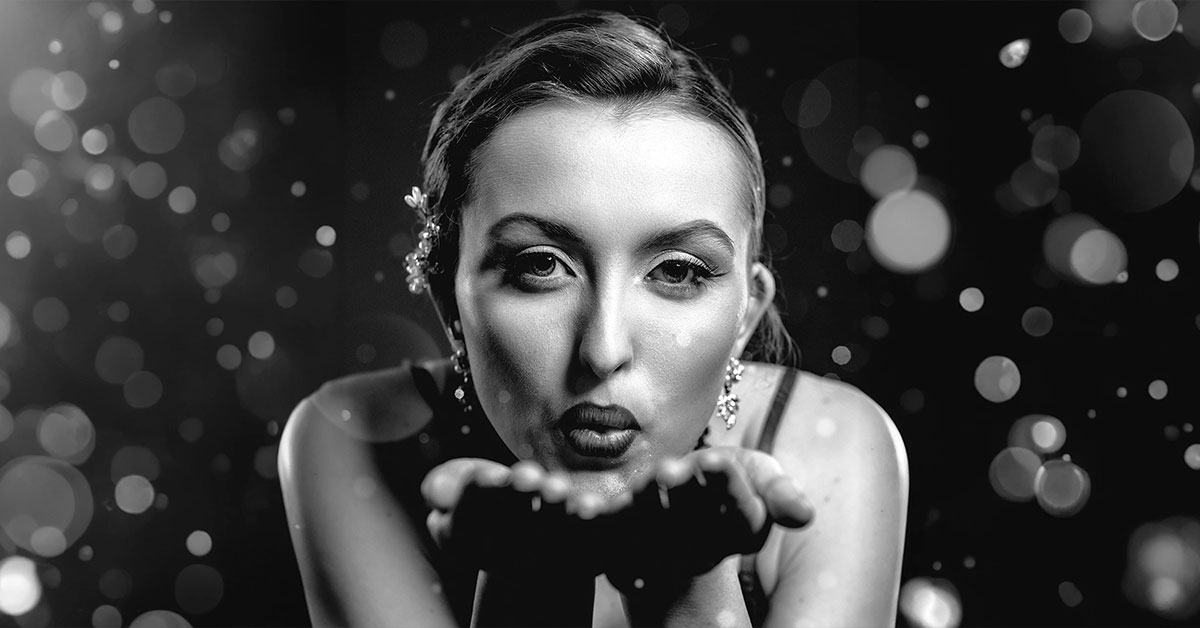Portrait serré de Kalysta soufflant des paillettes vers l’objectif, photo en noir et blanc réalisée en studio par Laurène Zabary.
