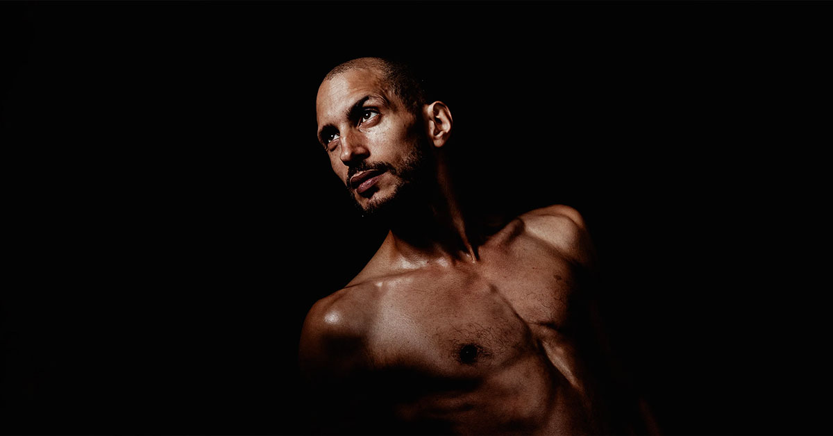 Portrait contrasté d’un comédien sur fond noir, regardant au loin avec intensité.