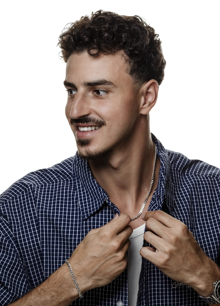 Portrait souriant de Noam ajustant sa chemise bleue pendant une séance book photo en studio à Paris.