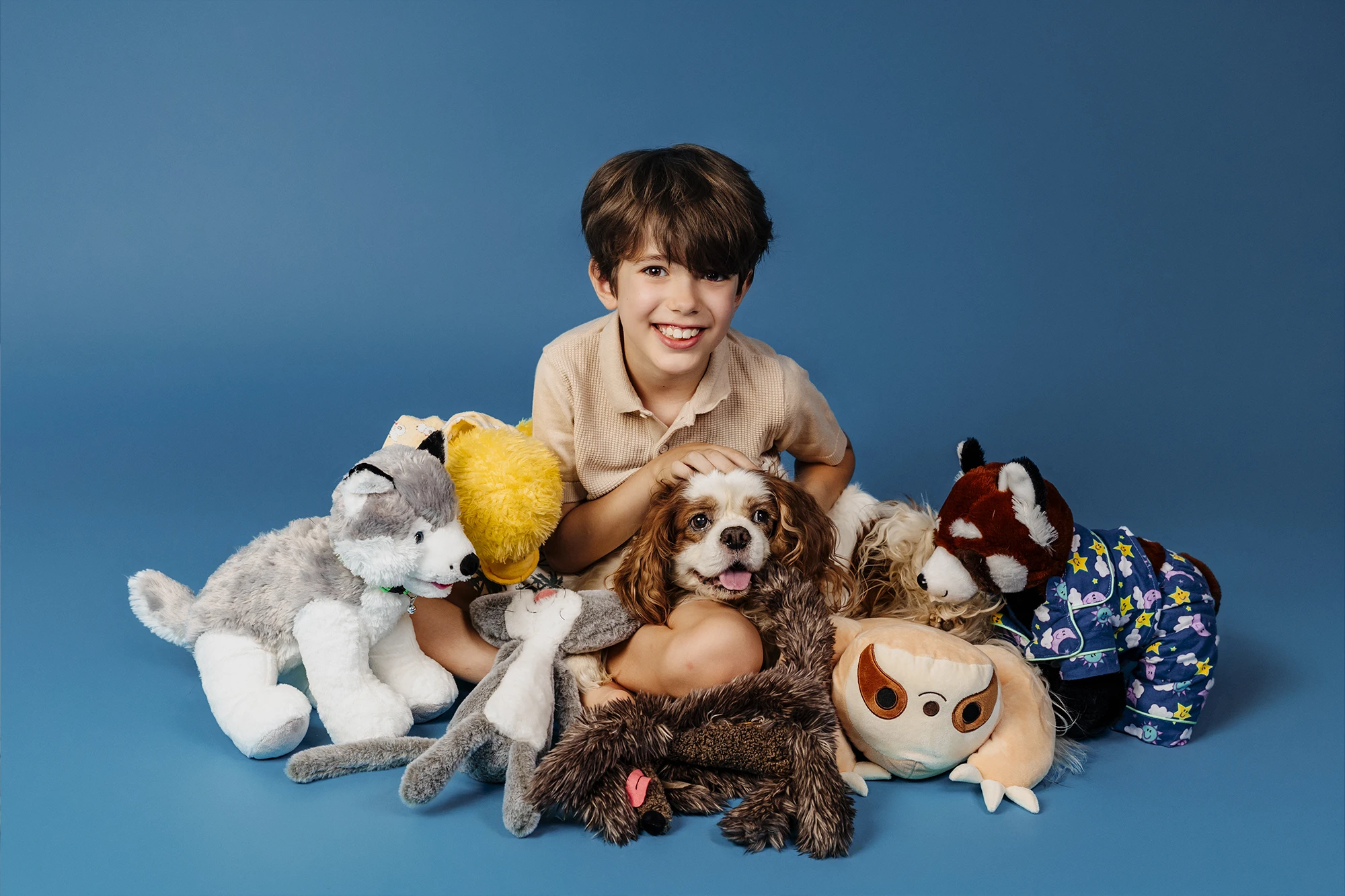 Un enfant pose avec Jäger et ses peluches sur un fond bleu lors d’une séance photo en studio à Paris.