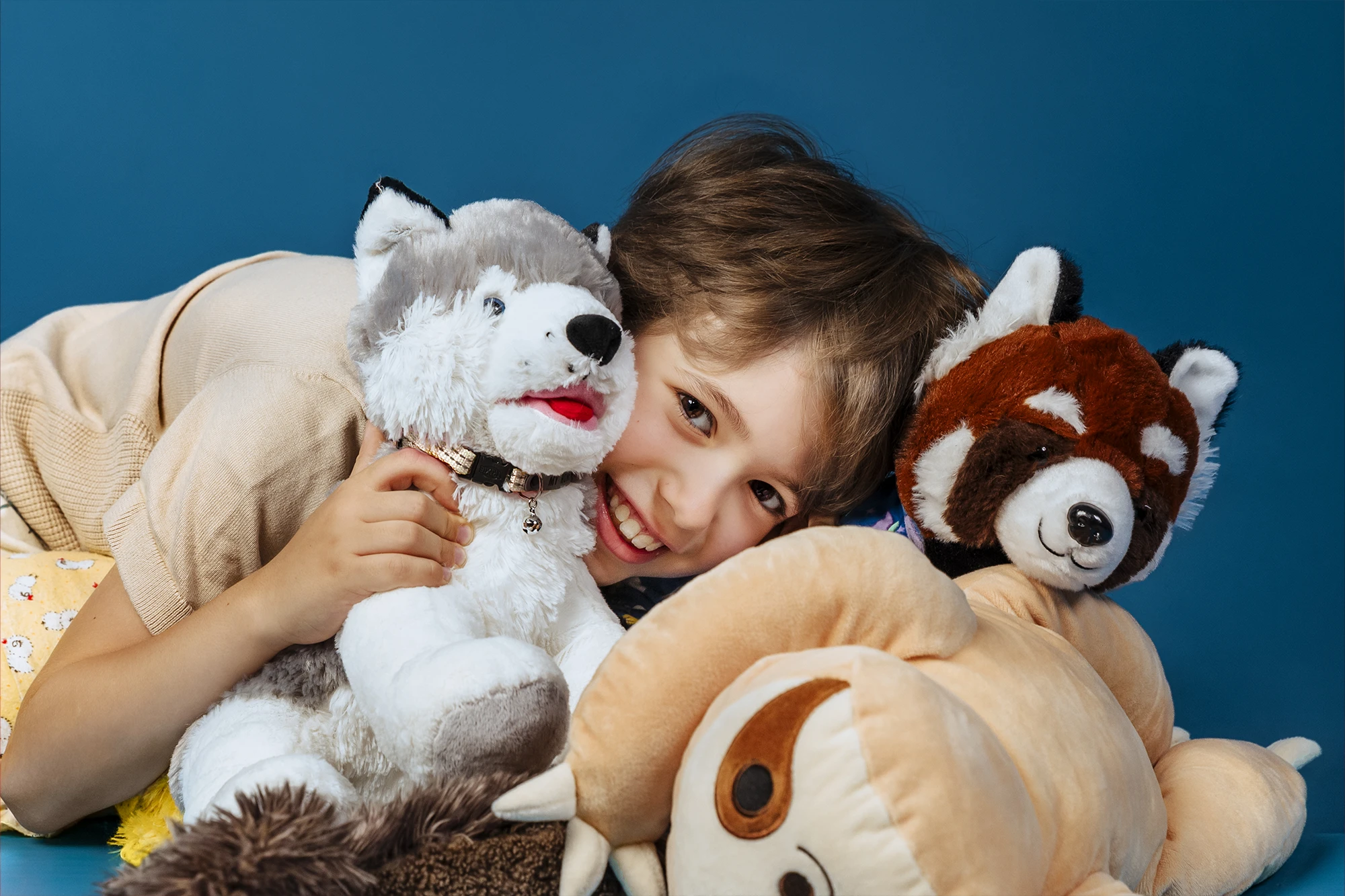 Portrait d’un enfant entouré de ses peluches sur fond bleu lors d’une séance photo en studio à Paris.